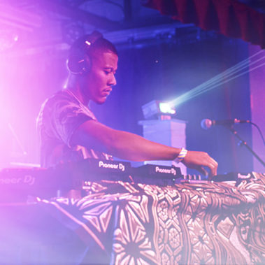 Focused DJ mixing tracks on a Pioneer DJ setup at a live club event with vibrant stage lighting